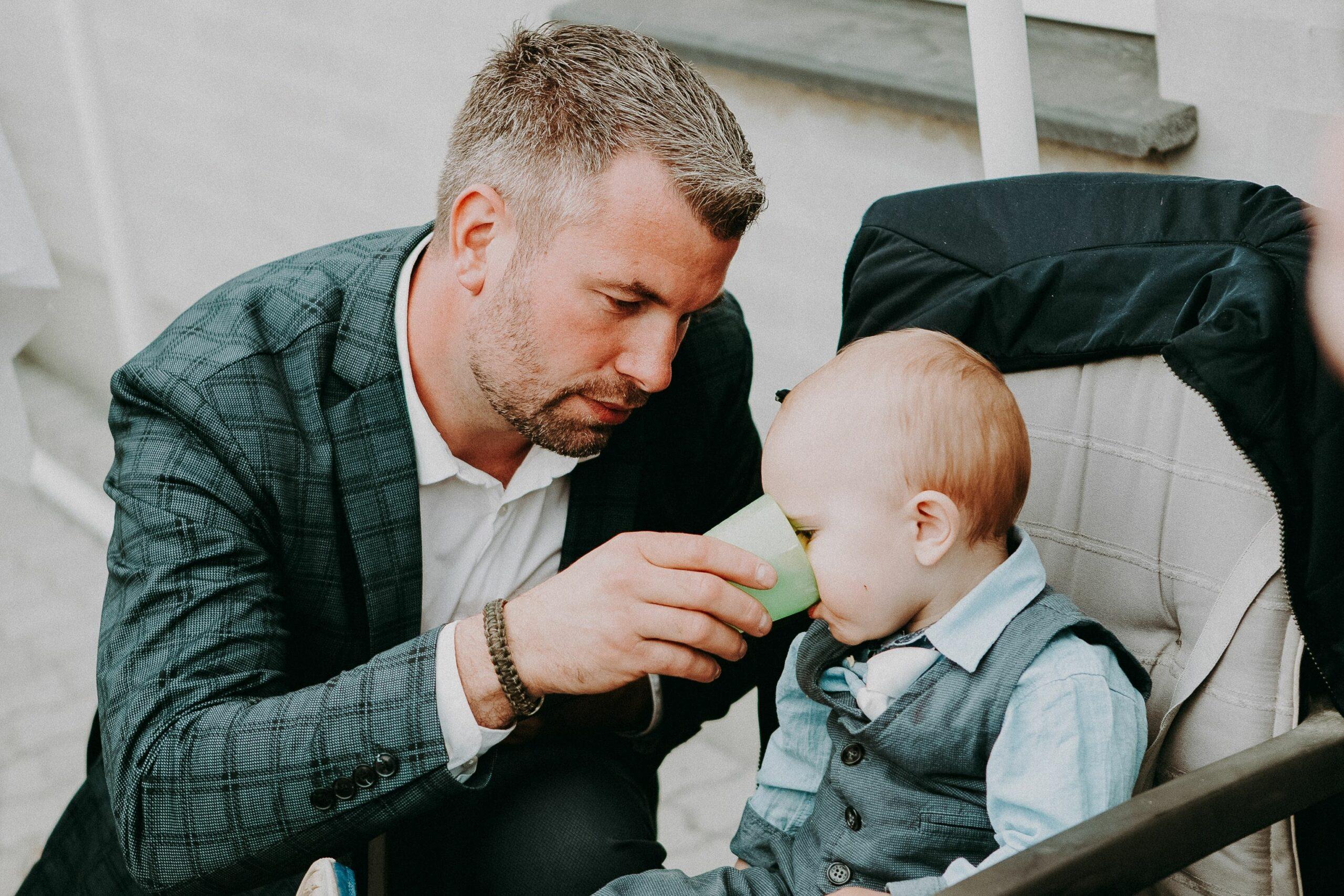 Father giving little child beverage in cup