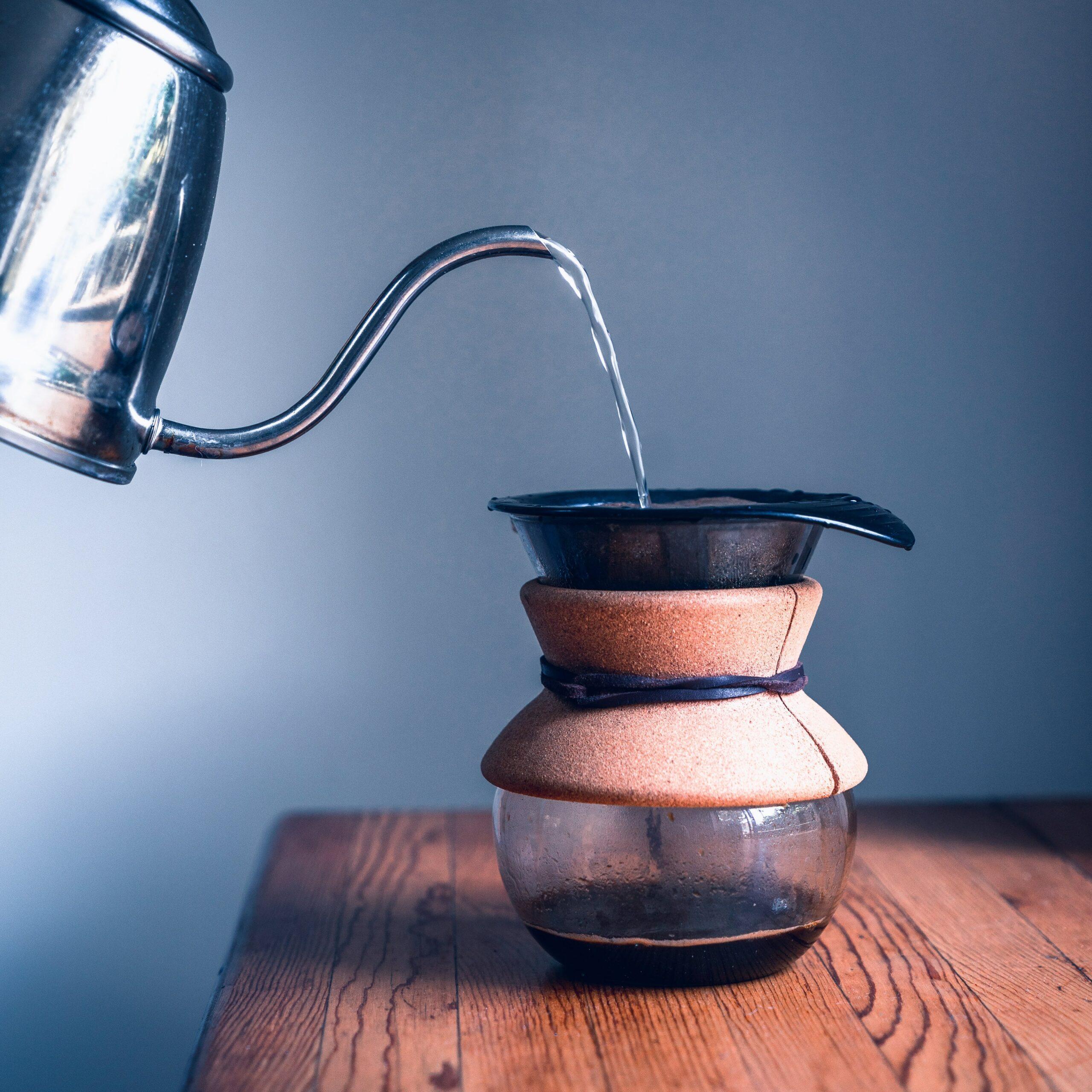 a kettle pouring boiling water over a pour over coffee maker